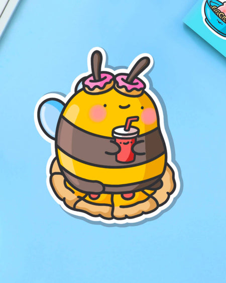 Cute cartoon-style vinyl sticker of a bumblebee with pink doughnut antennae, holding a red drink and sitting on a pie. Ideal for laptops, bottles, and journals.