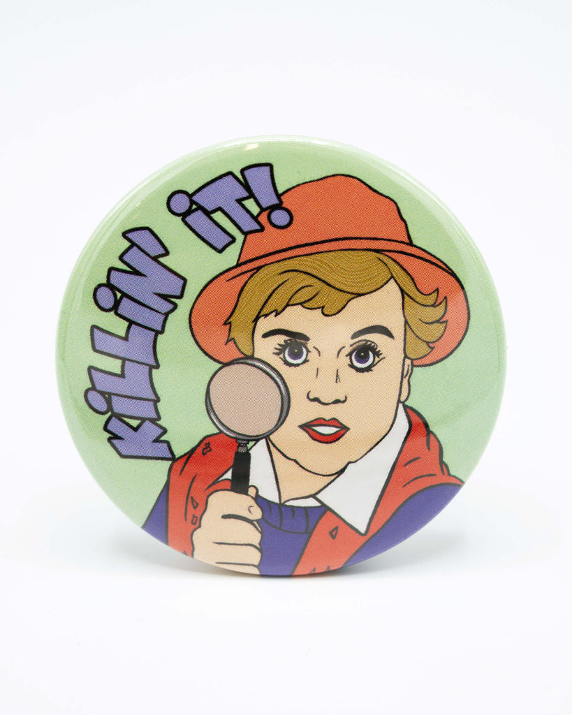 Pastel green round pocket mirror with an illustration of a murder she wrote character, jessica fletcher, holding a magnifying glass and blue bubble text that reads 'KILLIN' IT!'. Retro inspired design from Bite Your Granny.