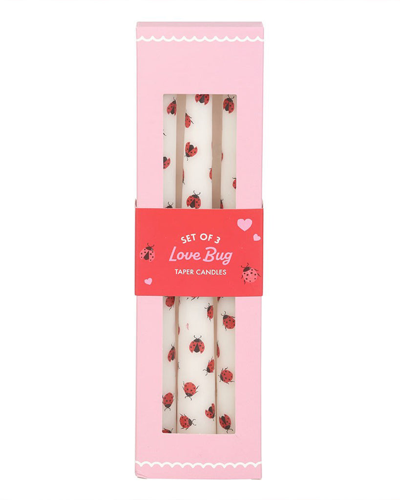 Hand holding the 3 Love Bug Ladybird Taper Candles against a pink cherry-print background. The playful ladybird pattern pops against the white wax, creating a fun, retro aesthetic.