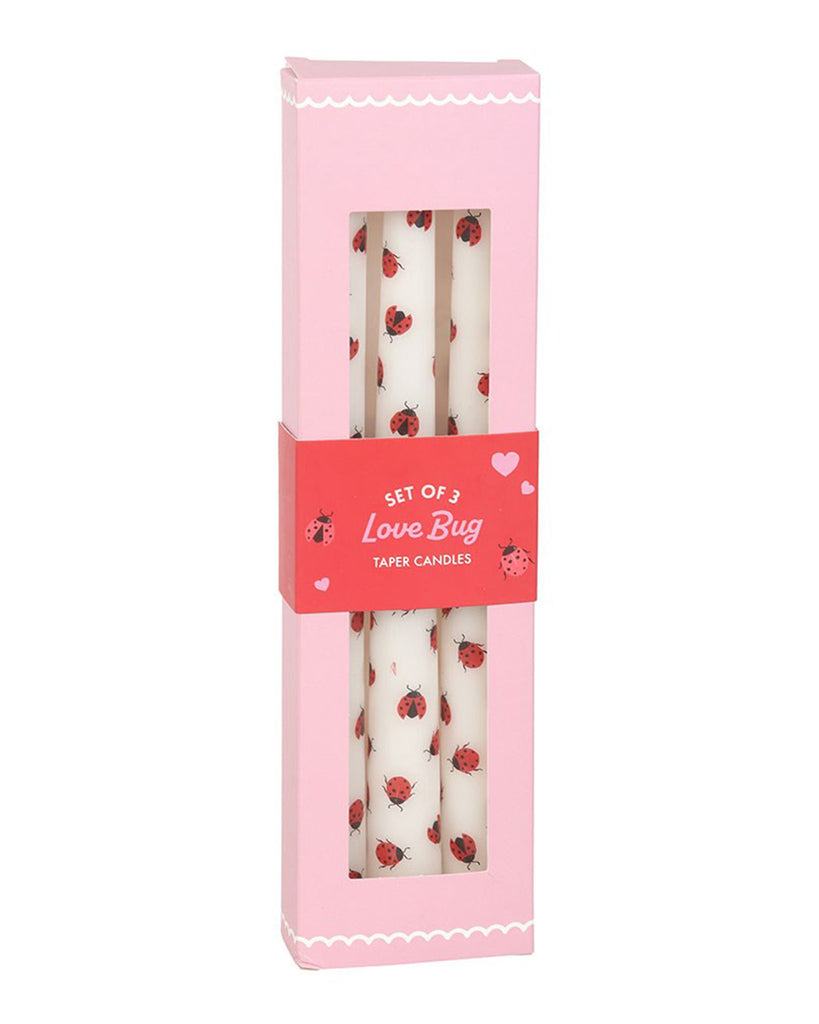 Front view of the boxed Love Bug Ladybird Taper Candles by Rebel Romance. The pink box features scalloped white detailing, heart illustrations, and a clear window showcasing the candles inside.