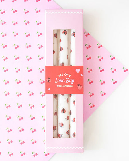 Set of 3 Love Bug Ladybird Taper Candles in pink packaging with a red label. The box has a clear window showing the white candles decorated with cute red and black ladybirds. Perfect for Valentine’s Day gifting or whimsical home decor.