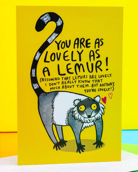 Bright yellow A6 greeting card by Rebel Romance featuring a hand-illustrated lemur with the message "You are as lovely as a lemur!" in playful black text. Designed by Katie Abey, the card includes quirky hand lettering and a whimsical lemur drawing with a striped tail, set against a cheerful background. Perfect for animal lovers and alternative stationery fans. Blank inside and printed in the UK.