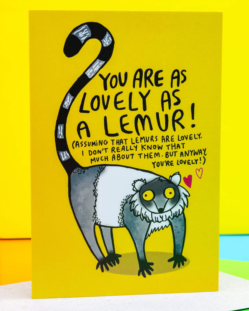 Bright yellow A6 greeting card by Rebel Romance featuring a hand-illustrated lemur with the message "You are as lovely as a lemur!" in playful black text. Designed by Katie Abey, the card includes quirky hand lettering and a whimsical lemur drawing with a striped tail, set against a cheerful background. Perfect for animal lovers and alternative stationery fans. Blank inside and printed in the UK.