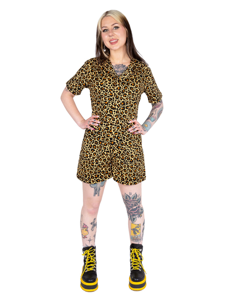 Florence stands facing forward wearing the Rebel Romance Classic Leopard Playsuit. The V-neckline, short sleeves, and signature leopard print pop against the white backdrop, styled with bold yellow boots.