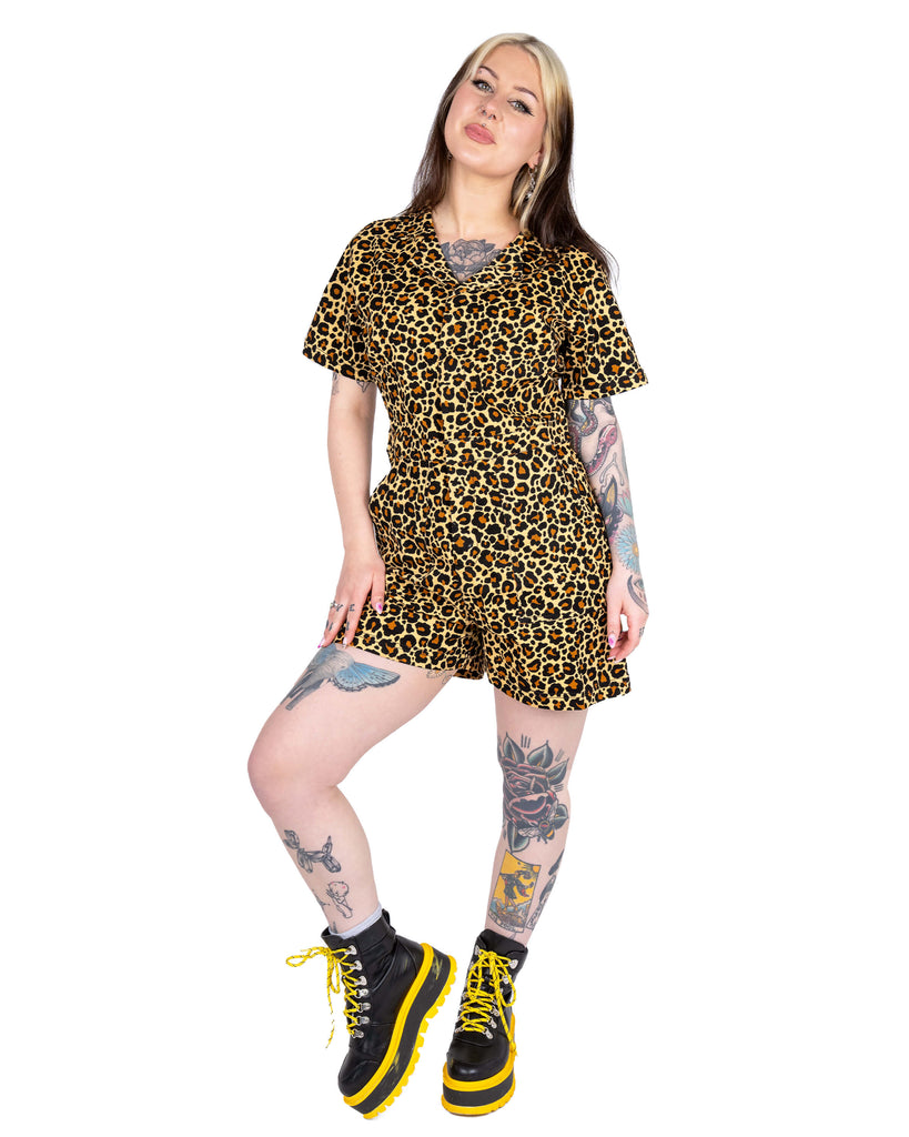 Model Florence poses with one leg bent in the Rebel Romance Classic Leopard Playsuit. The all-over leopard print and tailored fit offer a bold, retro feel. She pairs it with black and yellow platform boots.