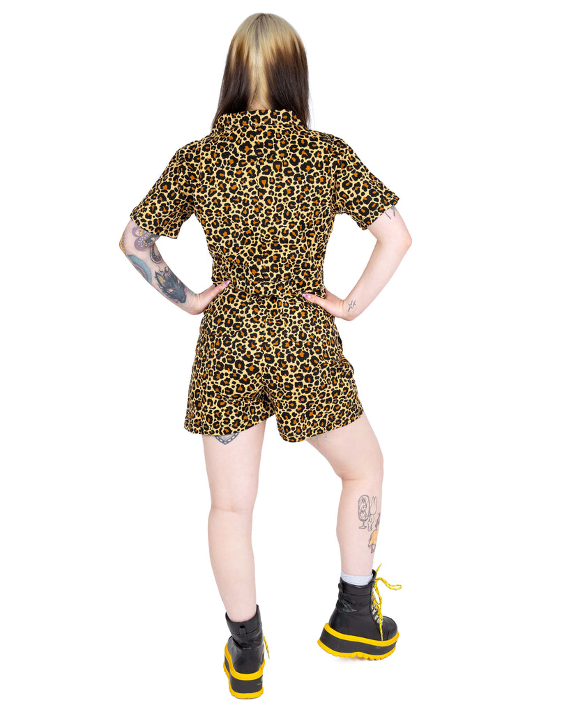 Model Florence stands with hands on hips showing the back view of the Rebel Romance Classic Leopard Playsuit. The collared neckline, short sleeves and flattering shape are visible, paired with yellow lace-up boots.