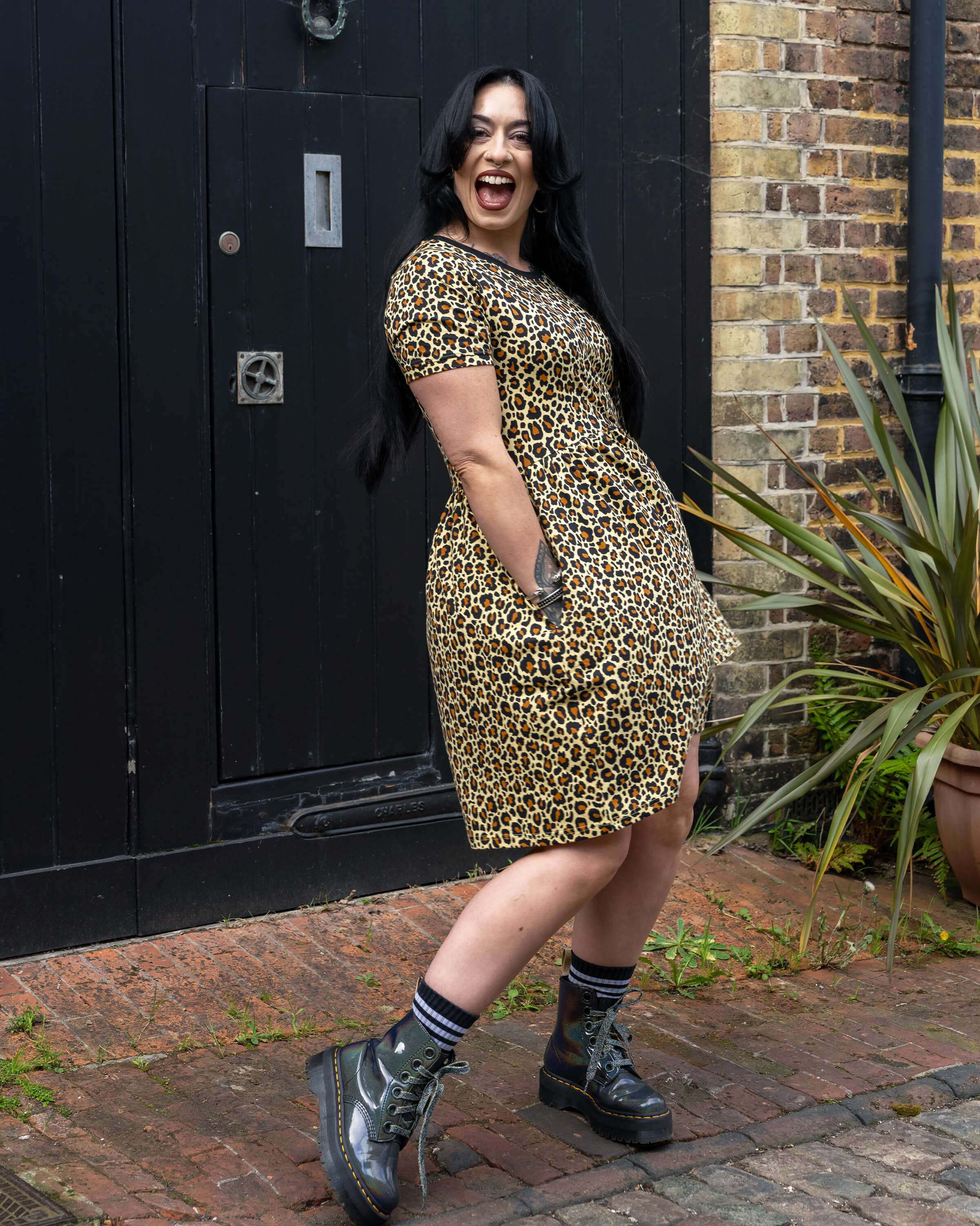 Side view of Carmen in the Rebel Romance Classic Leopard Print Smock Dress with hand in the pocket of the dress and a wide smile.