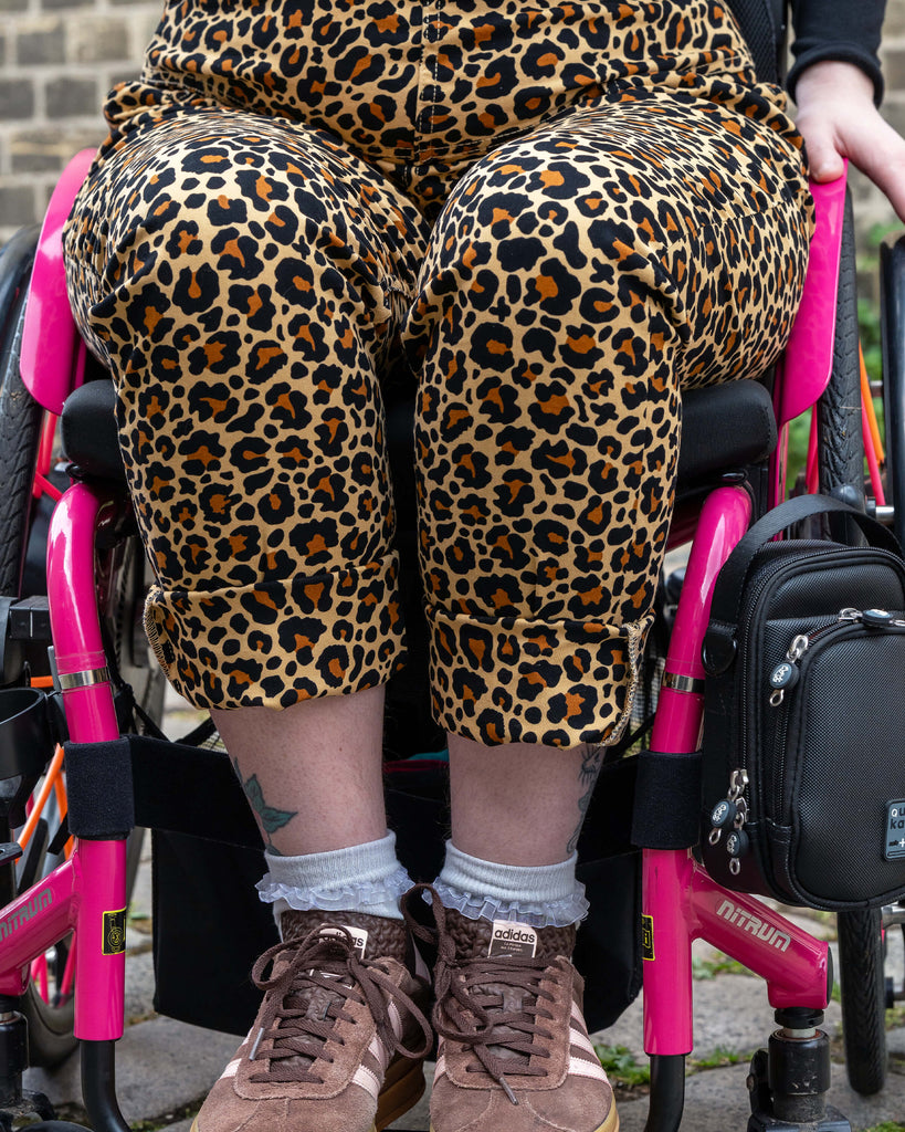 Detailed view of the rolled cuff legs of the Rebel Romance Leopard Print Dungarees worn by Eliza, paired with frilly socks and brown adidas trainers.