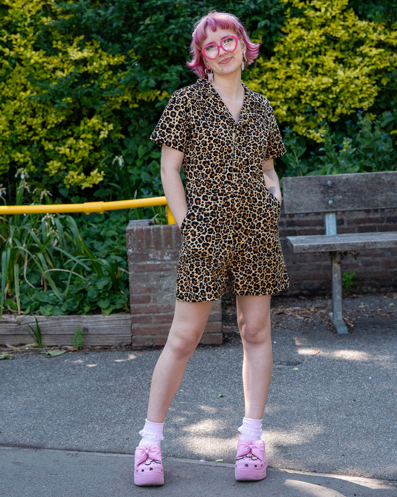 Full-length shot of Jess in the Rebel Romance Classic Leopard Playsuit standing confidently with hands in pockets. The alt-style leopard print romper is styled with pink socks and platform heels.