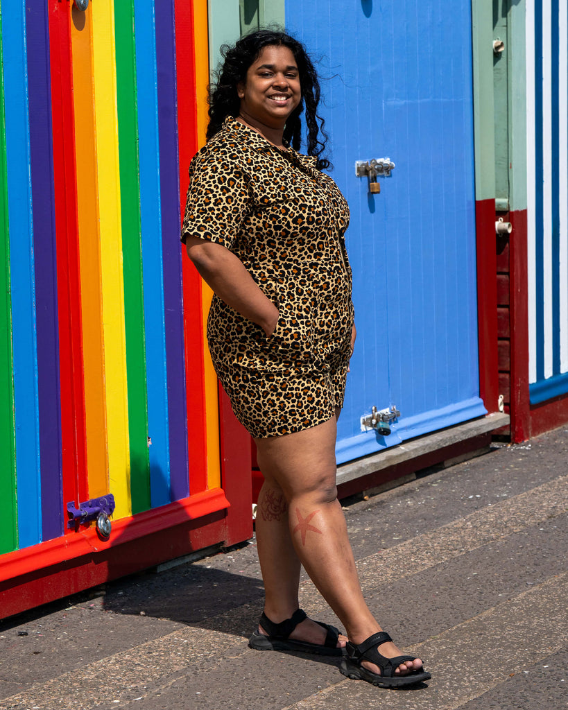 Model Vidhya turns slightly to show the back of the Rebel Romance Classic Leopard Playsuit on Brighton’s pebbled beach. Her curly hair and the sea breeze bring the leopard print look to life.