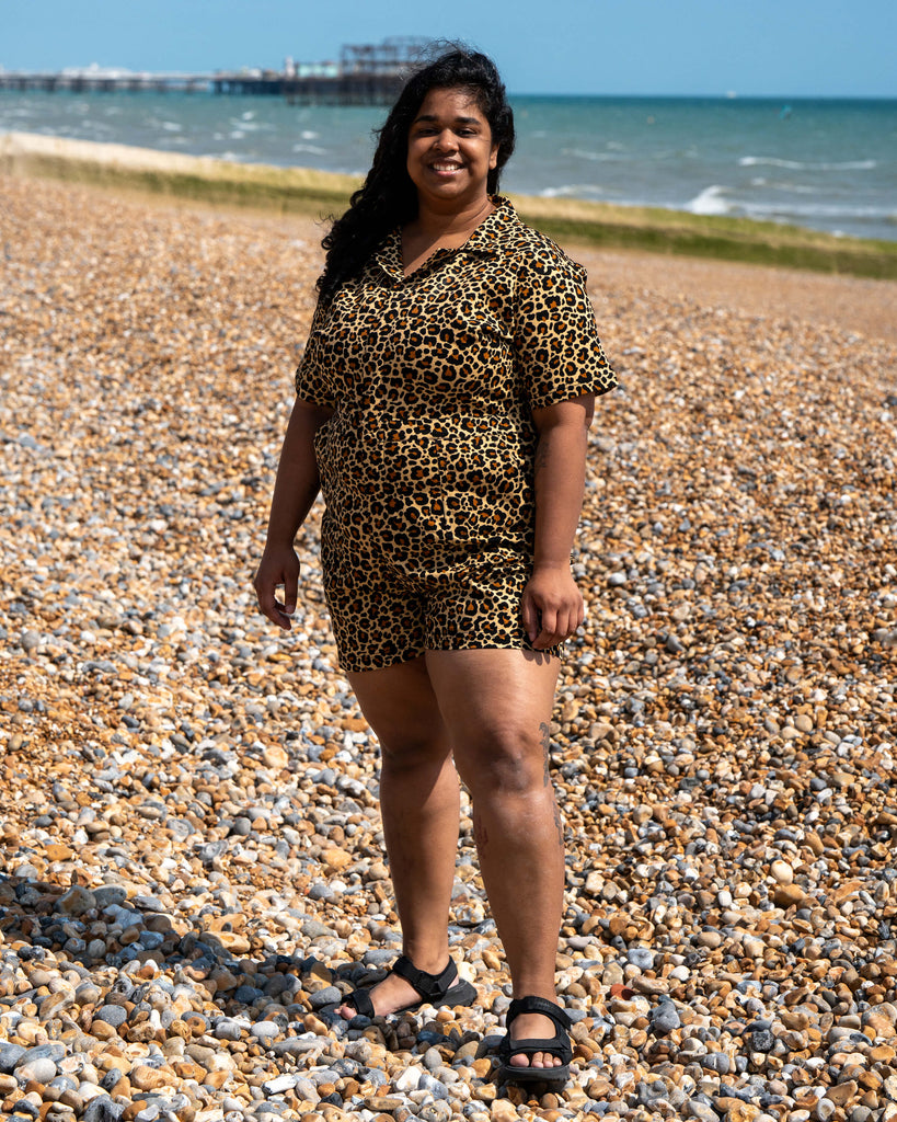 Full-length image of Vidhya on Brighton beach wearing the Rebel Romance Classic Leopard Playsuit. With the sea and West Pier behind her, she models the bold, alt-style leopard romper.