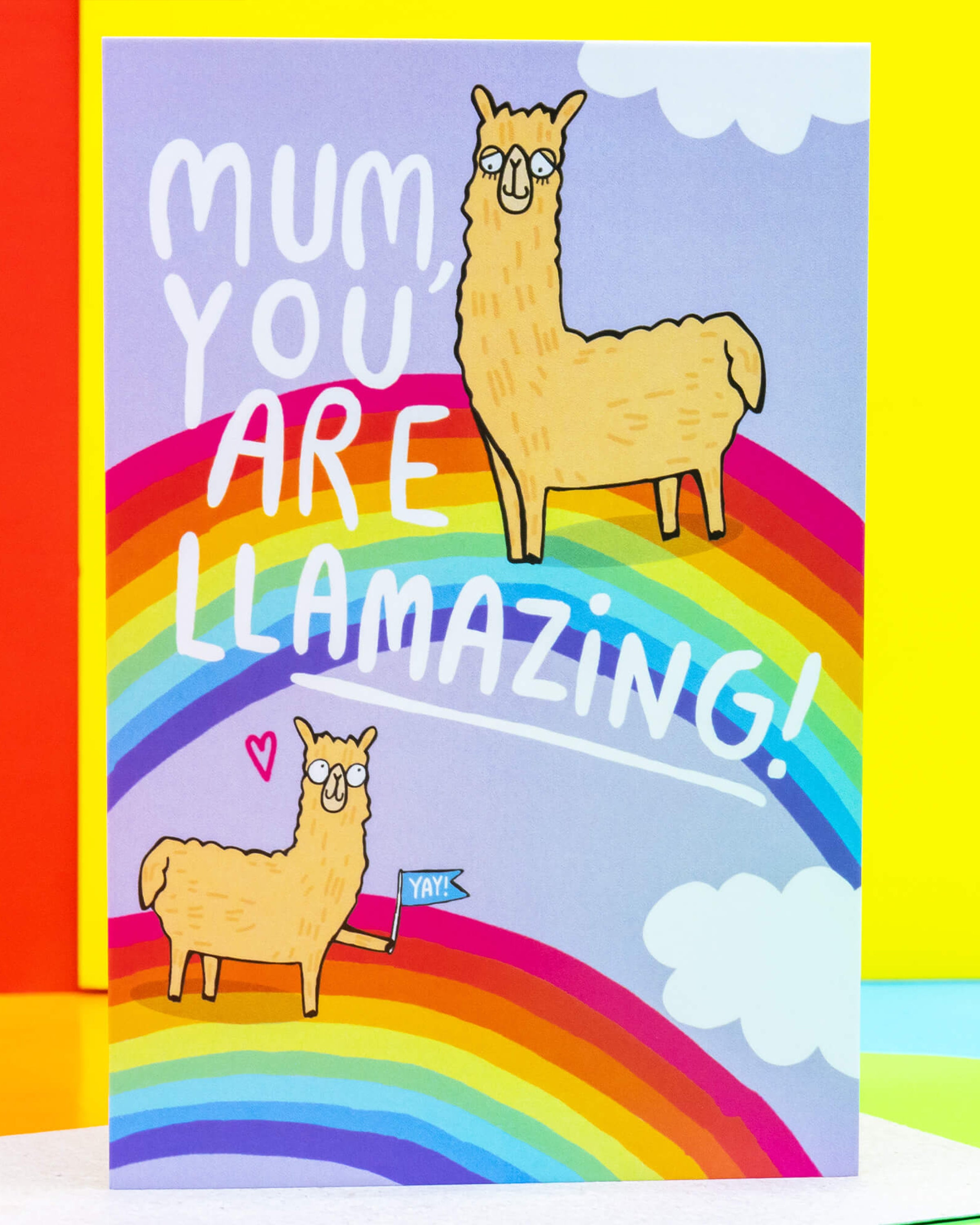 A colourful A6 greeting card by Katie Abey from Rebel Romance featuring two illustrated llamas on a rainbow background with the text “Mum, You Are Llamazing!” in playful white lettering. One llama holds a “Yay!” flag, and a pink heart floats beside it. A bright, feel-good card for mums who deserve a smile.