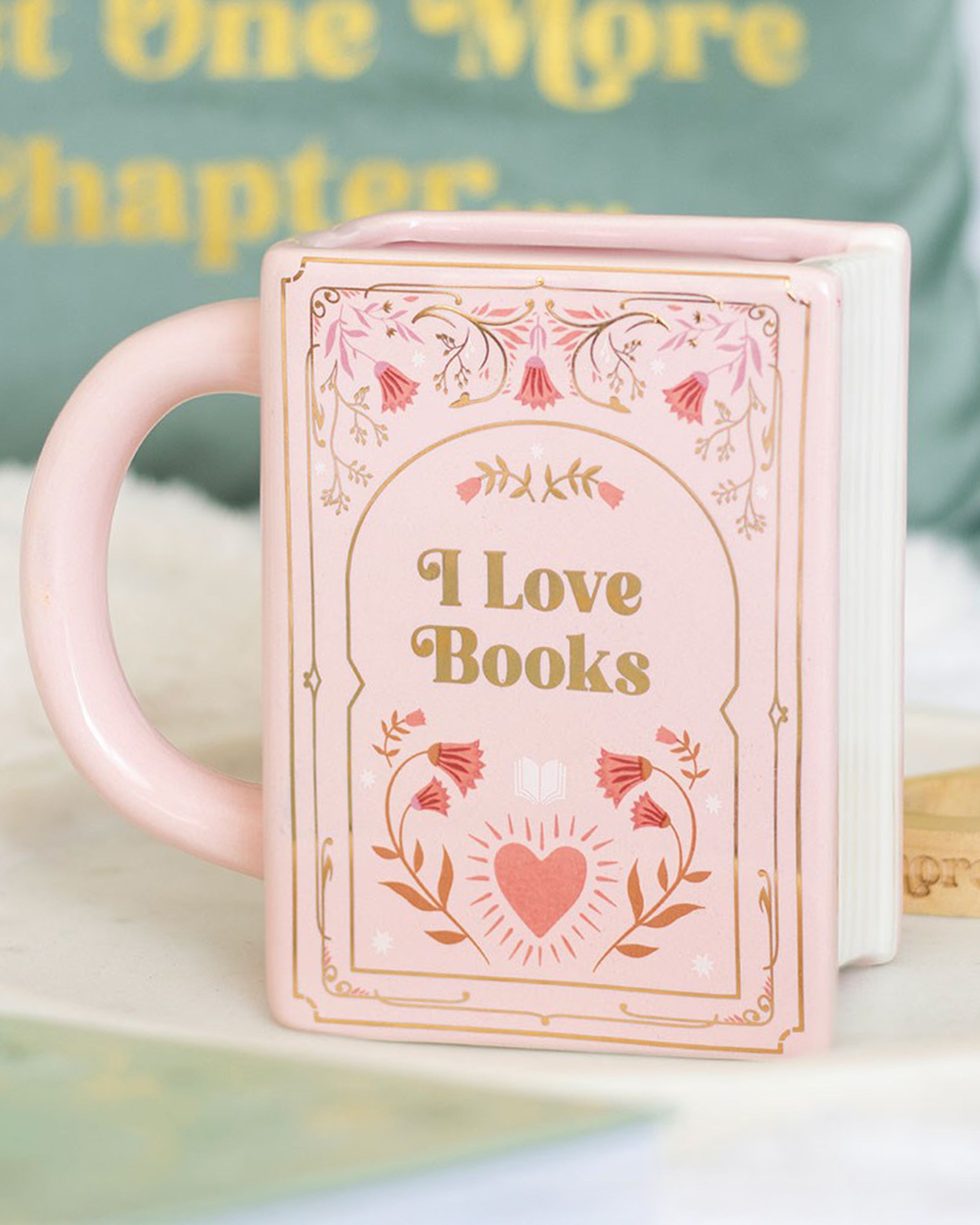 Lifestyle photo of the Rebel Romance “I Love Books” pink ceramic mug shaped like a book, styled with cosy home décor. A fun, literary-inspired gift for tea and coffee lovers.
