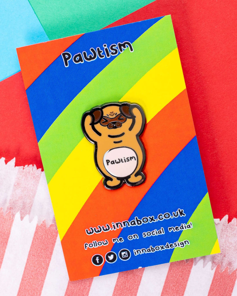 The Pawtism Dog Enamel Pin displayed on its colourful backing card with a rainbow background. The word “Pawtism” is printed at the top, and the pin features a brown pug with raised paws and a gentle expression. Sold by Rebel Romance, a UK brand championing alternative style and inclusivity.