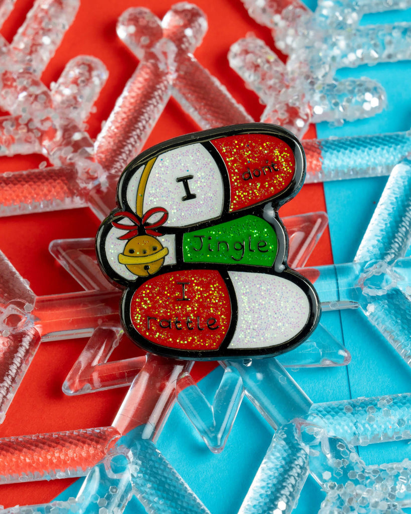 Glittery festive enamel pin with a pill design reading “I Don’t Jingle, I Rattle”, placed on a snowflake-shaped decoration. Designed by Innabox and sold by Rebel Romance, a small UK business known for quirky gifts, enamel pins, and alternative fashion.