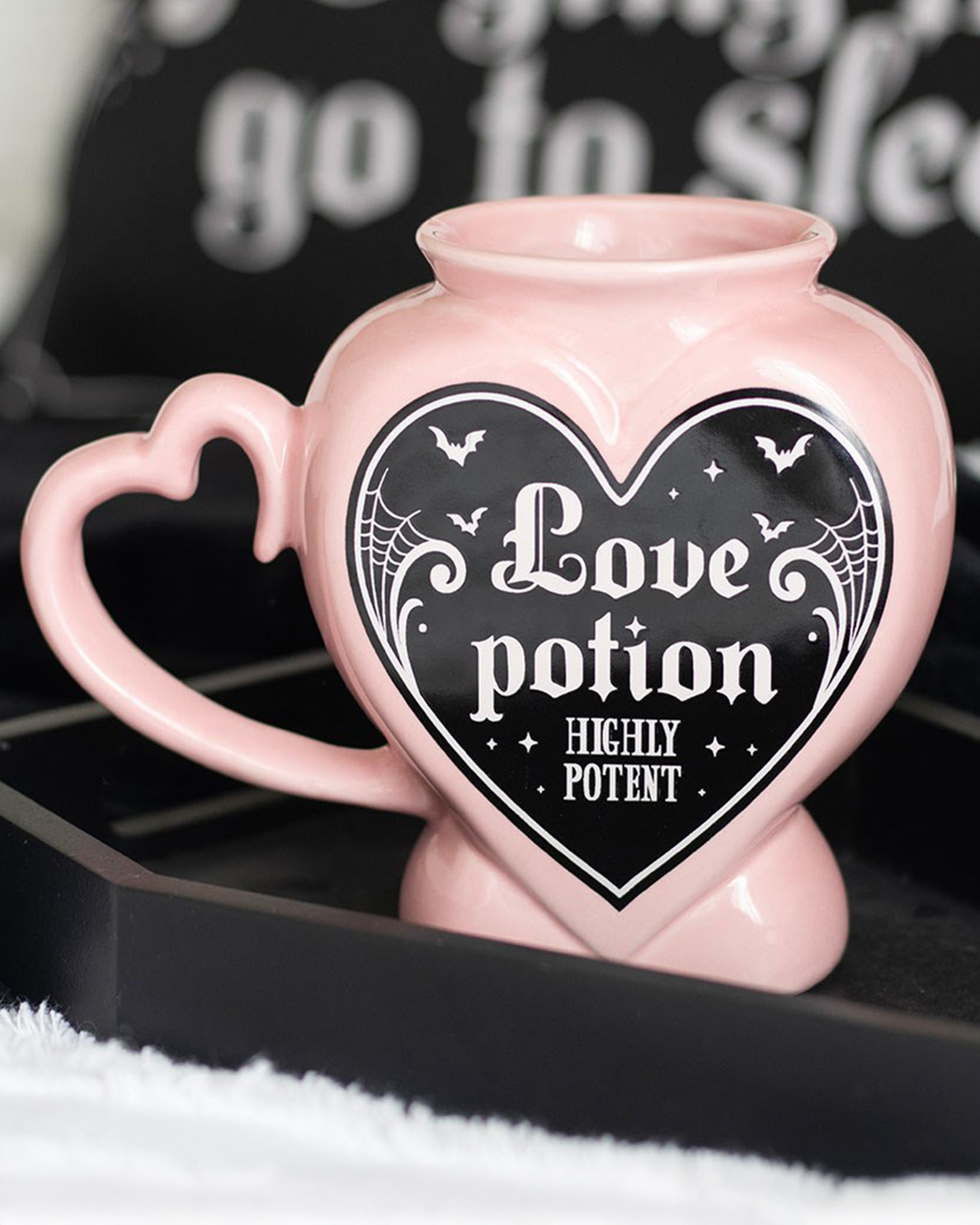 Close‑up styled shot of the Rebel Romance Love Potion Shaped Mug in pink with gothic detailing, placed on a black tray with cosy accessories. Perfect alternative homeware for witchy and gothic aesthetics.