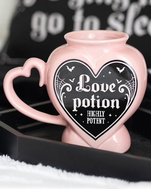 Close‑up styled shot of the Rebel Romance Love Potion Shaped Mug in pink with gothic detailing, placed on a black tray with cosy accessories. Perfect alternative homeware for witchy and gothic aesthetics.