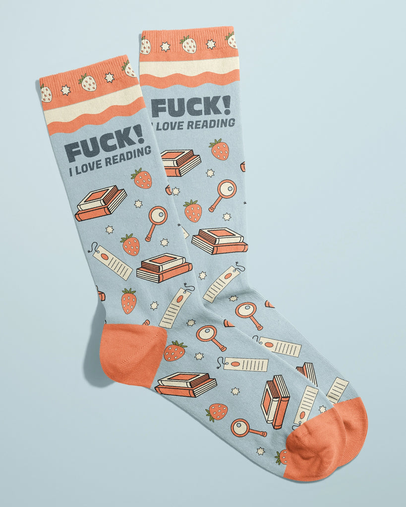 Rebel Romance novelty socks by FUN CLUB laid side-by-side with visible slogan “FUCK! I LOVE READING” in bold lettering. Socks feature strawberries, books, bookmarks, magnifying glasses, and stars on a pastel blue background with orange cuffs and toes.