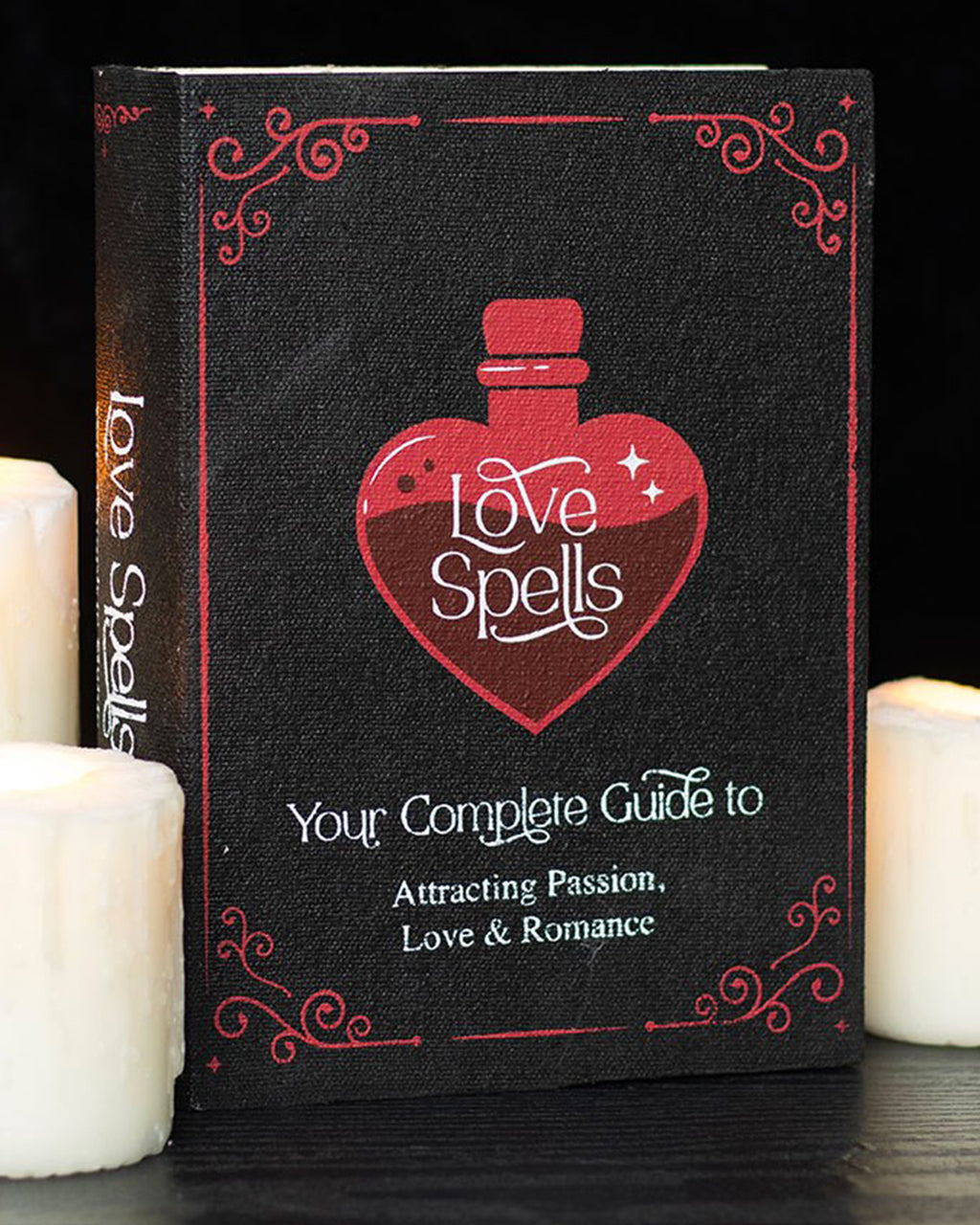 A black storage box designed to look like a vintage ‘Love Spells’ book, with a red heart-shaped potion bottle and gothic text on the cover. The box is open to show a hollow interior for storing small items like jewellery or trinkets.