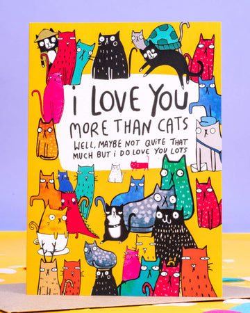 A colourful A6 greeting card from Rebel Romance featuring quirky illustrated cats in vibrant colours surrounding the text "I love you more than cats – well, maybe not quite that much but I do love you lots." Designed by Katie Abey, this playful card is perfect for cat lovers. Printed on yellow background with multicoloured cartoon cats. Ethically made in the UK by a small business celebrating alternative fashion and bold designs.