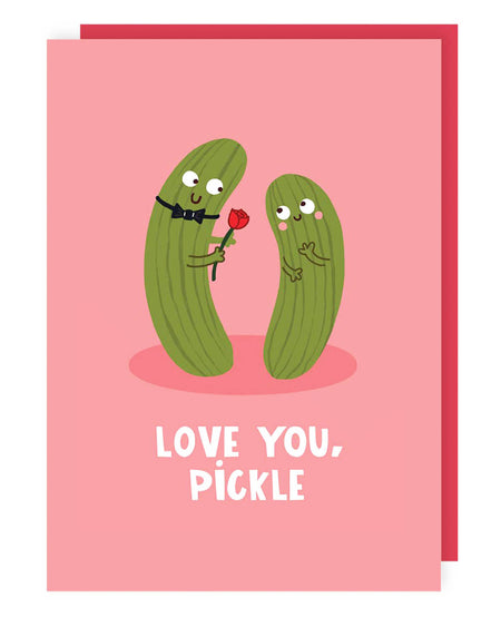 A pink greeting card with two illustrated pickles; one wearing a bow tie and holding a red rose, the other blushing. The words “LOVE YOU, PICKLE” are printed in white below. A red envelope is included.
