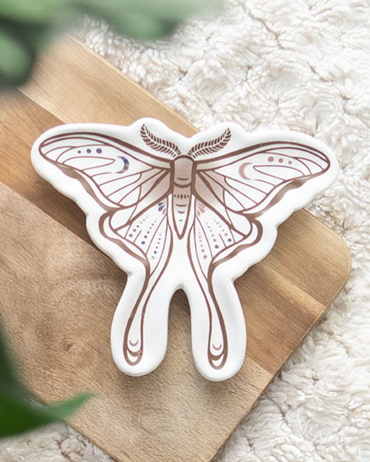 A ceramic luna moth trinket dish by Rebel Romance, shaped like a moth with delicate wing details in earthy brown and soft purple tones. Styled on a wooden board and cosy textured fabric, perfect for holding jewellery, coins or keys.