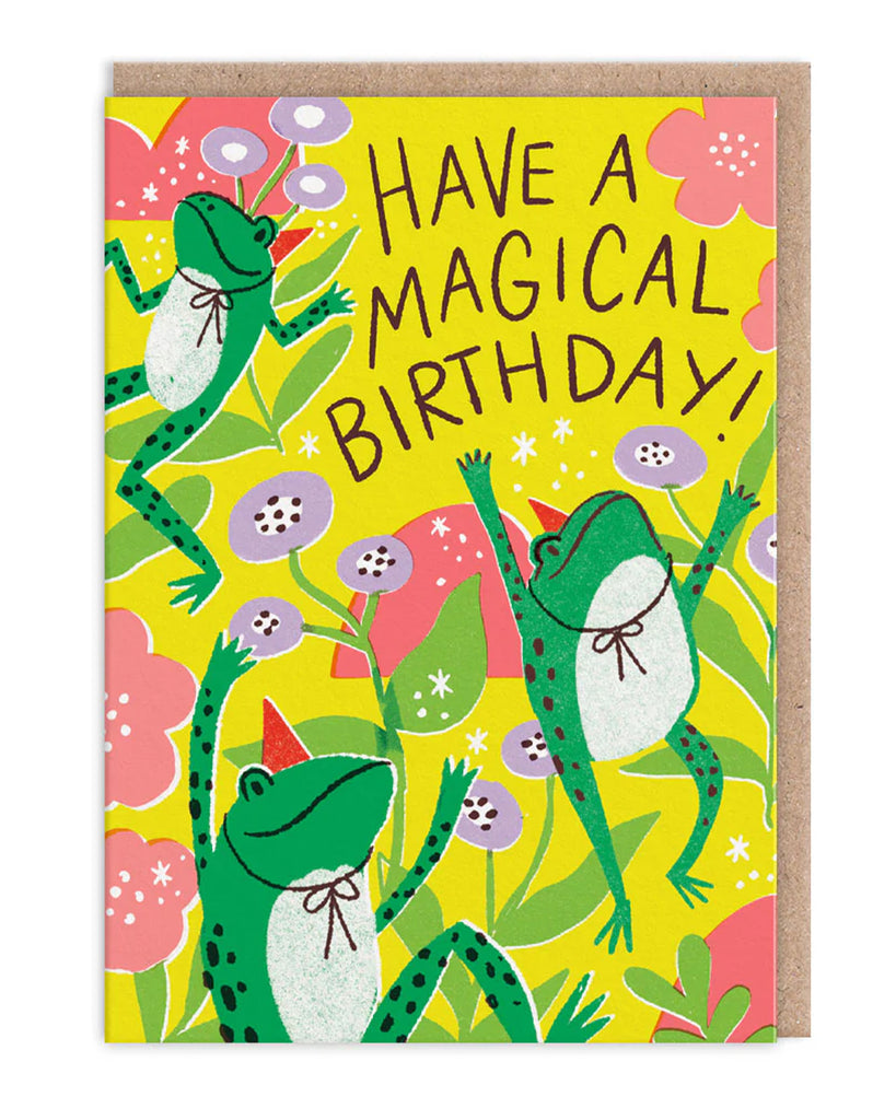 A colourful A6 birthday card featuring three green frogs with red party hats and white bellies, dancing among bright flowers and leaves. The neon yellow background is decorated with pink and purple floral illustrations, with the text "Have a Magical Birthday!" in bold, playful lettering. A fun and whimsical design by Hello!Lucky, available from Rebel Romance, a UK brand celebrating quirky and alternative style.