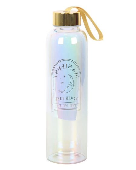 A tall, iridescent glass water bottle with a gold screw-top lid and soft yellow carry loop. The front features a crescent moon and stars with the phrase "Manifest Your Life – Creative Fuel" in shimmering gold print.
