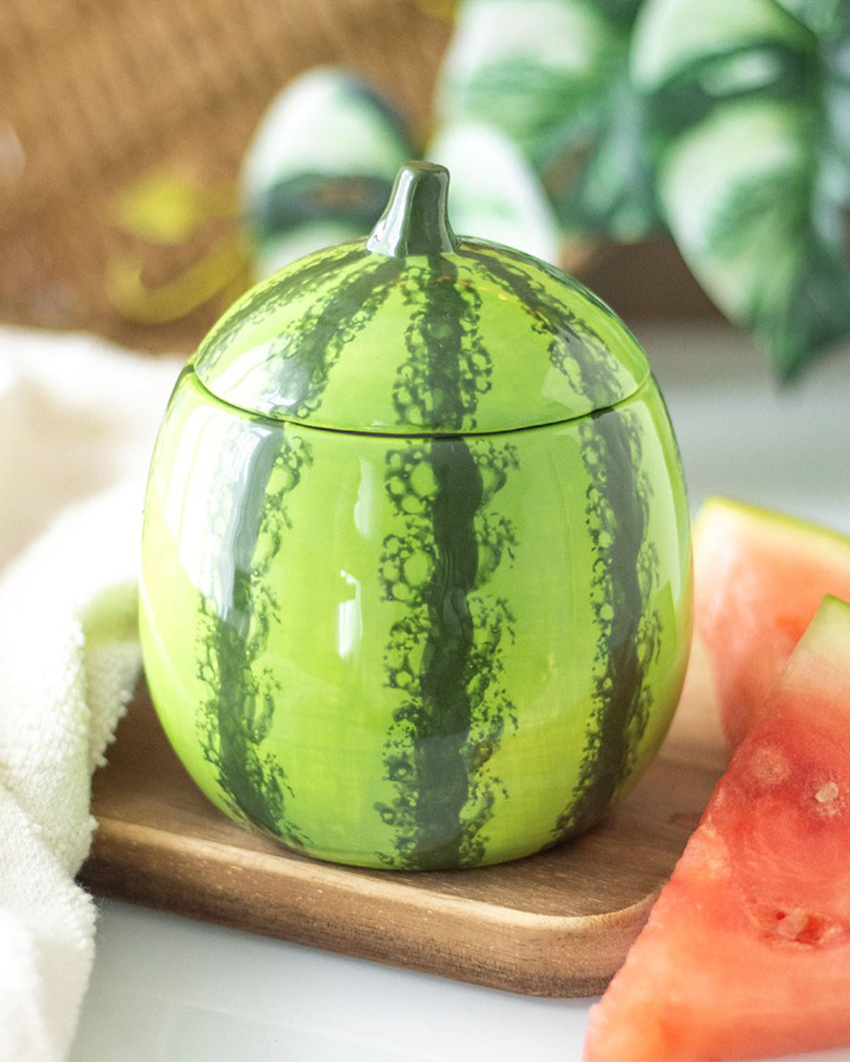The watermelon candle jar styled on a wooden surface, surrounded by fresh watermelon slices. Its detailed fruit-inspired design makes it a playful and decorative piece.