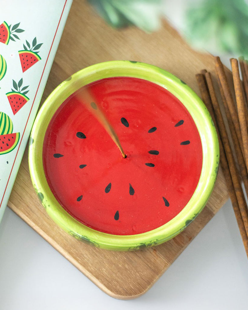 A stylishly staged photo of the watermelon incense holder on a wooden surface, with incense sticks beside it and a leafy background, adding a fresh and fruity aesthetic to home decor.