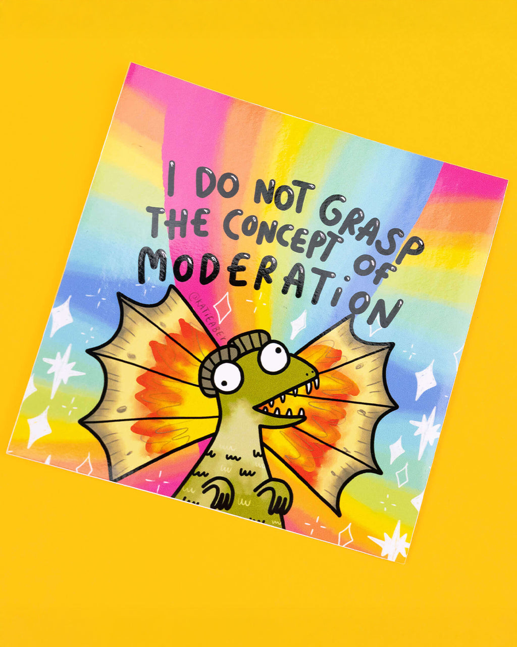 A colourful square vinyl sticker designed by Katie Abey, sold by Rebel Romance. It features a wide-eyed dinosaur with dramatic frilled wings against a bright rainbow background. The bold black text above reads: “I Do Not Grasp The Concept Of Moderation.” A playful, loud design perfect for maximalists, chaos gremlins, and sticker lovers alike.