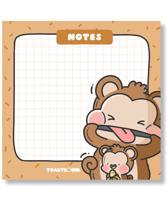 Flat lay of Toastedink monkey sticky notes on a blue background with a pink pen. Features cheeky cartoon monkeys and a gridded note space. Available at Rebel Romance, a UK indie store for whimsical and retro stationery lovers.