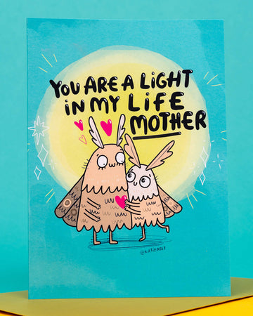 Bright and quirky A6 greeting card by Rebel Romance featuring two illustrated moth characters hugging under a glowing light with the text “You Are A Light In My Life Mother.” Designed by Katie Abey, this colourful card is perfect for Mother’s Day, birthdays, or to show appreciation. Printed in the UK on 250gsm card with a blank inside for personal messages.