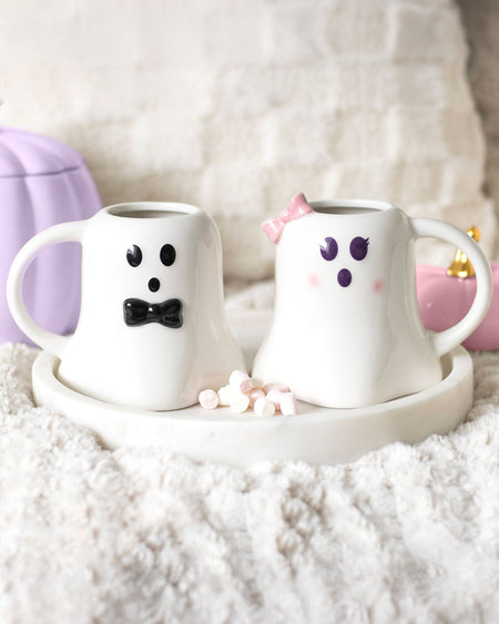 A cosy aesthetic featuring the Mr and Mrs Boo ghost mug set from Rebel Romance, placed on a plush, fluffy surface with a white tray. The wedding themed mugs, designed with a cute ghostly theme, are accompanied by pastel pumpkins and mini marshmallows for a charming, spooky vibe.