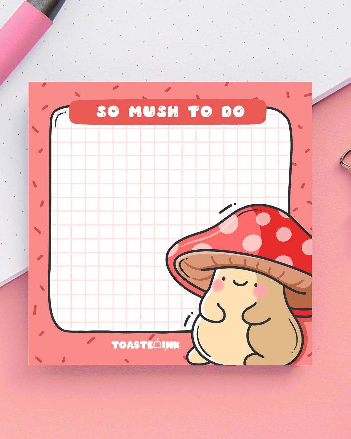 A square sticky note pad with a red border and grid paper design, featuring a cute, blushing mushroom character with a red and white spotted cap in the bottom right corner. The top header reads “So Mush To Do” in bold white text. A fun and functional memo pad for everyday reminders.