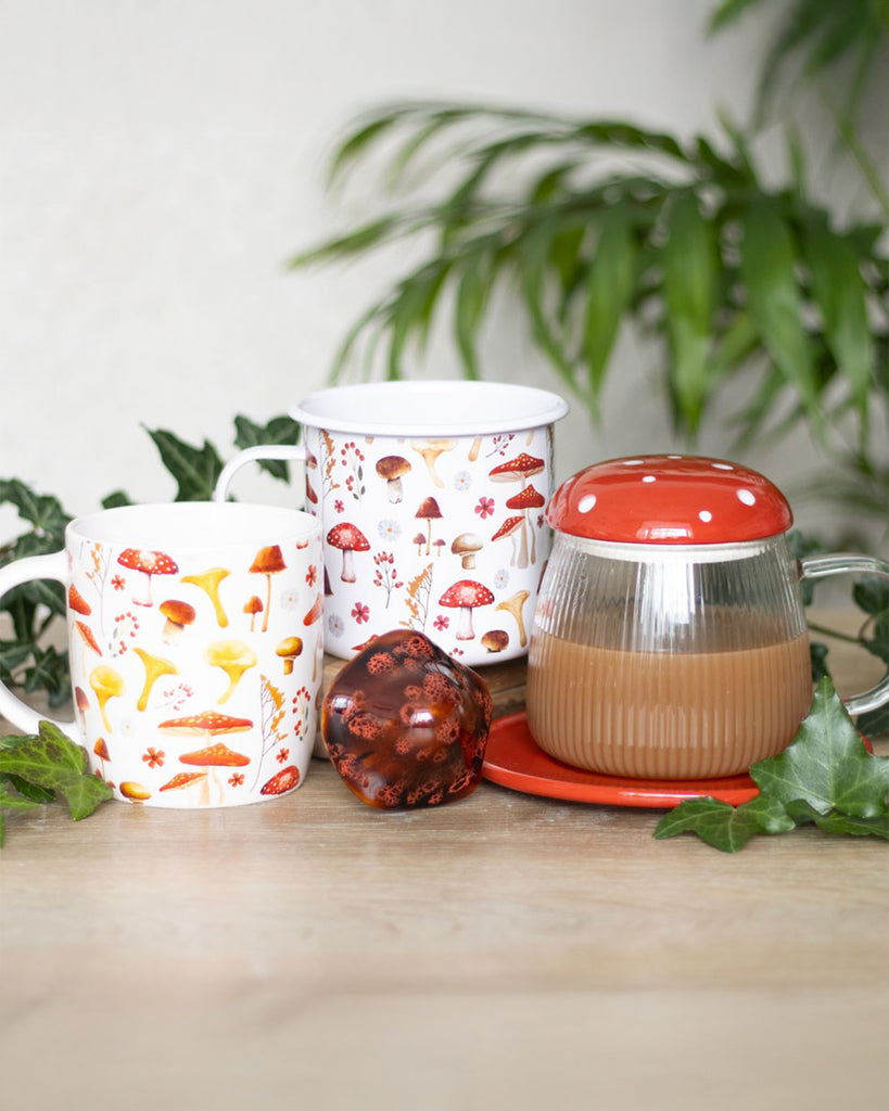 A cosy woodland-themed tea setup featuring two Rebel Romance mushroom print mugs, a red-topped mushroom-shaped glass teapot, and autumnal greenery. A perfect scene for nature lovers and fungi enthusiasts.