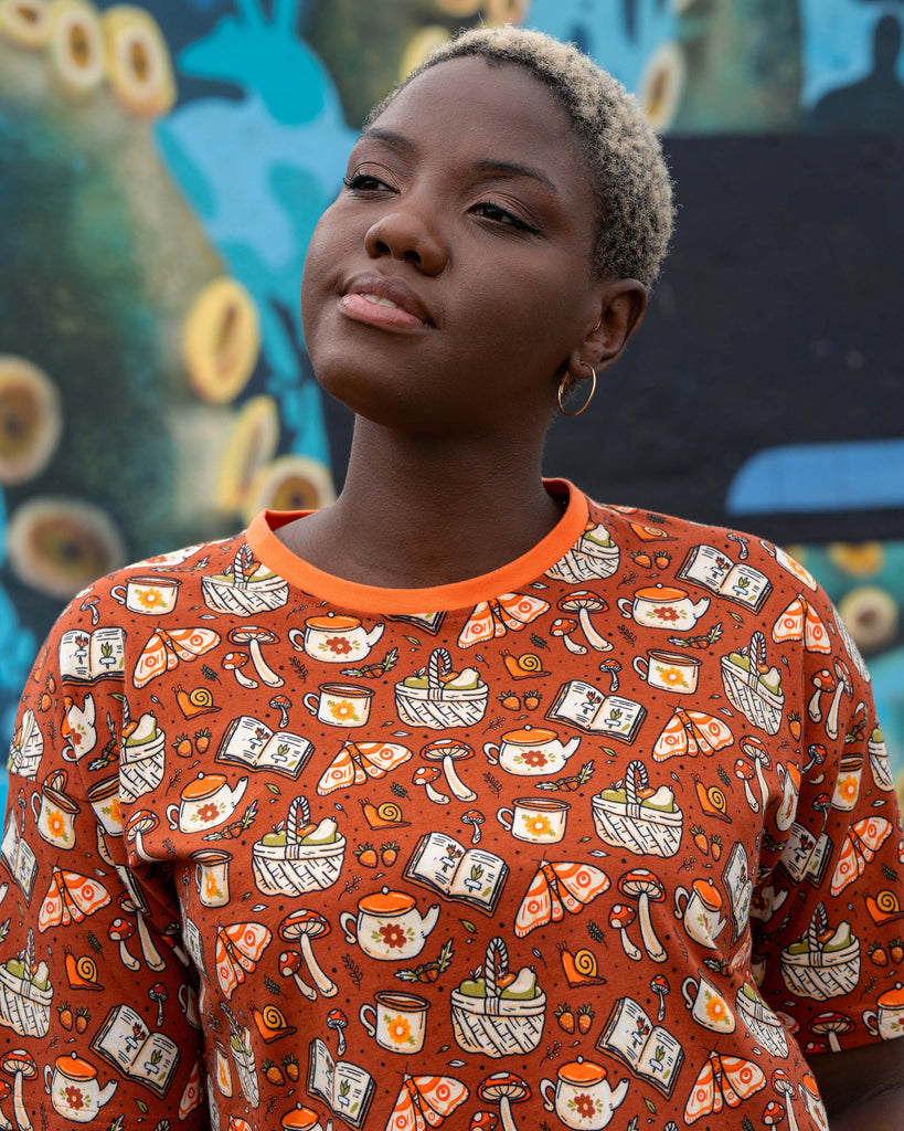Side view of Chish wearing the Rebel Romance Mushroom Tea Party boxy cropped tee, styled with hoop earrings and black jeans.