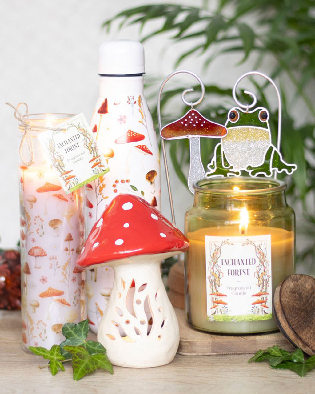 A whimsical woodland-themed display featuring the All Over Mushroom Print Metal Water Bottle by Rebel Romance. The white bottle is covered in colourful toadstools and botanical details, nestled among candles, ivy, and other enchanted forest décor.