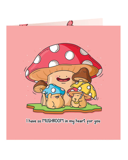 Front view of a pink square greetings card featuring a large happy toadstool surrounded by smaller colourful mushrooms with animal-like faces. Text reads “I have so MUSHROOM in my heart for you.” A cute, pun-filled card designed by Toastedink and available from Rebel Romance in the UK.
