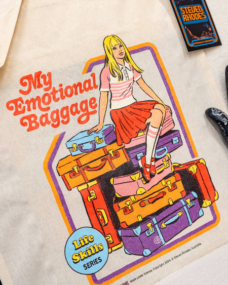 A natural fabric tote bag featuring Steven Rhodes’ retro-style “My Emotional Baggage” design. The illustration shows a blonde girl sitting on a pile of colourful suitcases with the words “My Emotional Baggage” in bold red letters. Playful and self-aware, this tote combines a quirky aesthetic with functionality.