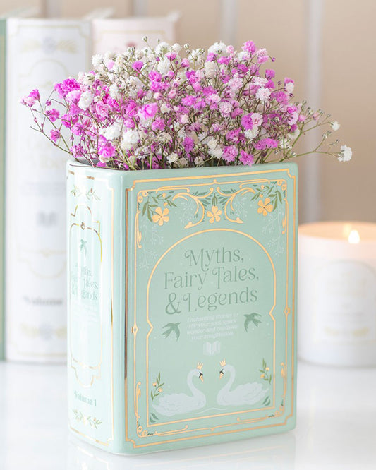 Styled display of the Rebel Romance Myths, Fairy Tales & Legends Green Book Shaped Vase filled with pink and white flowers. A ceramic vase shaped like a book, perfect for bookworms, fantasy lovers, or anyone who wants to add a whimsical literary flourish to their home.
