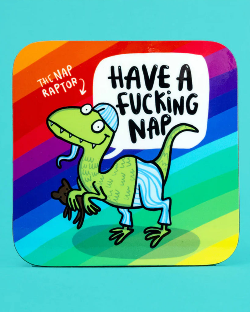 Colourful coaster featuring a green dinosaur wearing striped pyjamas and a nightcap, holding a teddy bear. The rainbow background includes the text “Have a f*cking nap” in a white speech bubble, and “The Nap Raptor” in the corner.
