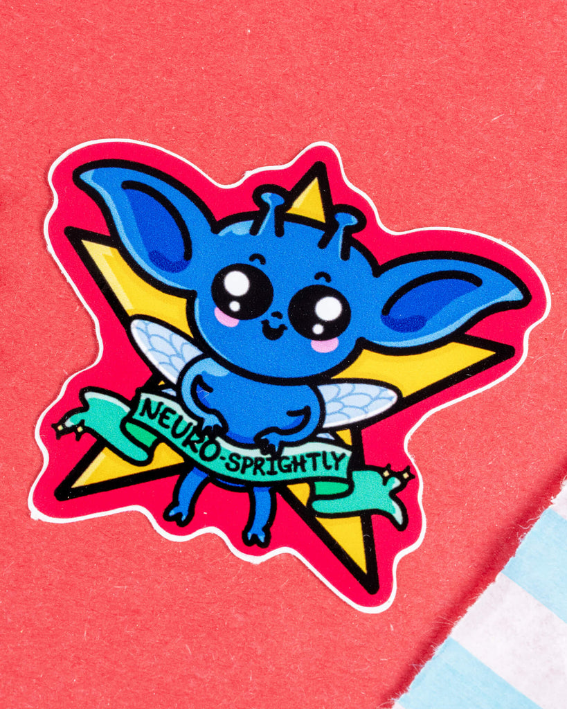 Glossy vinyl sticker featuring a blue sprite character with fairy wings, big ears, and sparkly eyes, holding a banner that reads "Neuro-Sprightly". Designed by Innabox and sold by Rebel Romance, a small UK brand that embraces neurodivergence and alternative style. Sticker is shaped like the character and set against a bold starburst background. Perfect for laptops, notebooks or water bottles.