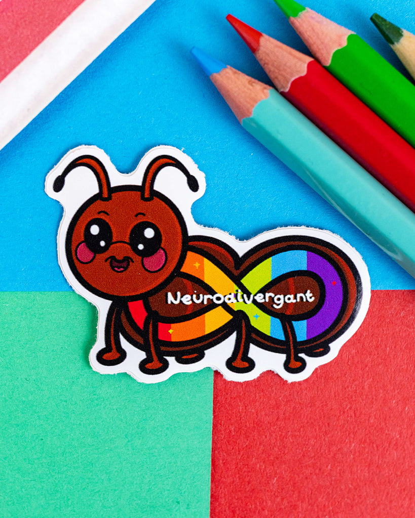 Neurodivergant Ant Sticker by Innabox, available from Rebel Romance. Cute cartoon-style ant with a smiling face and infinity symbol body in rainbow colours. Features the word "Neurodivergant" across its body. Surrounded by colourful pencils and a red eraser on a bright, multicoloured background. Perfect for laptops, water bottles, and journals. A playful and inclusive vinyl sticker celebrating neurodiversity.