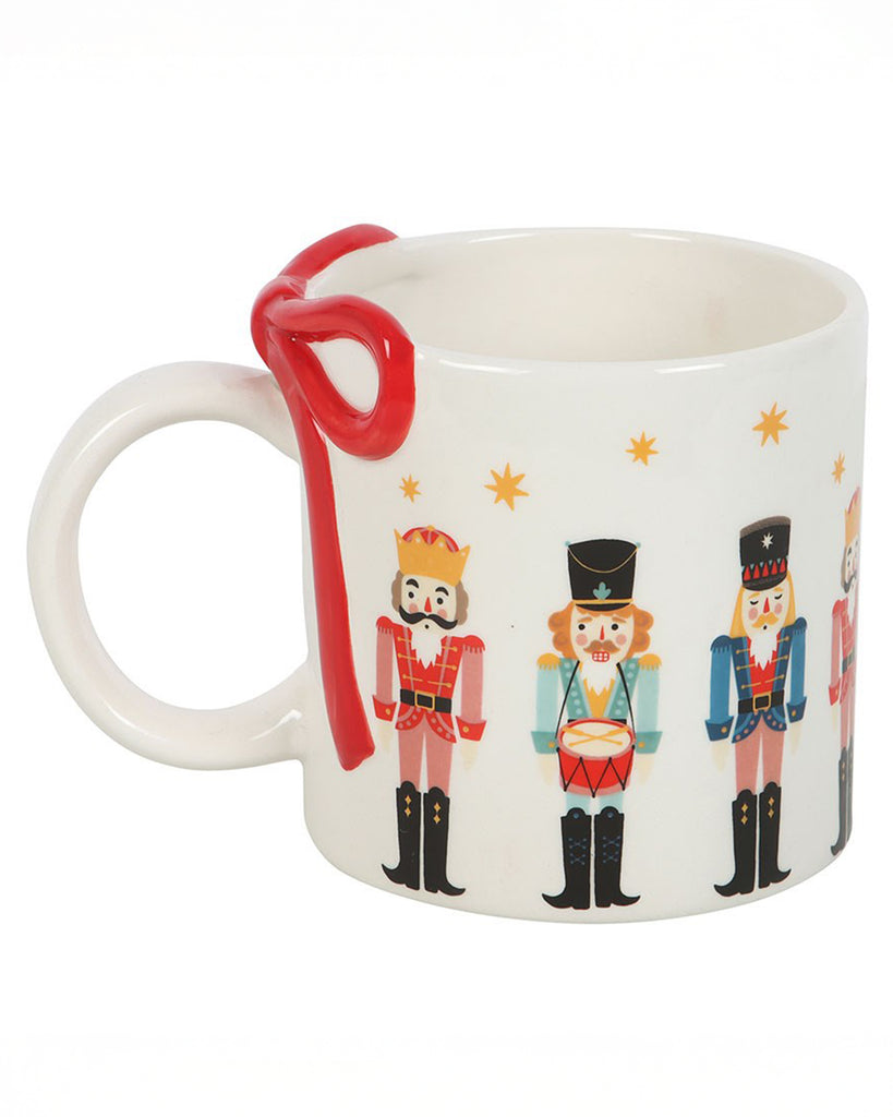 Side angle of the Rebel Romance festive Nutcracker Print Mug, showcasing the charming nutcracker illustrations and red bow handle on a plain white background.