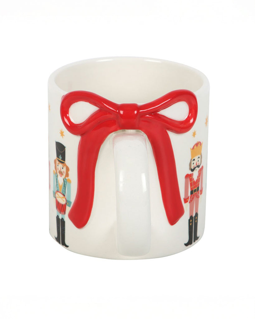 Back view of the Rebel Romance Nutcracker Print Mug showing the 3D red bow detail on the handle with illustrated nutcracker soldiers and orange star accents.