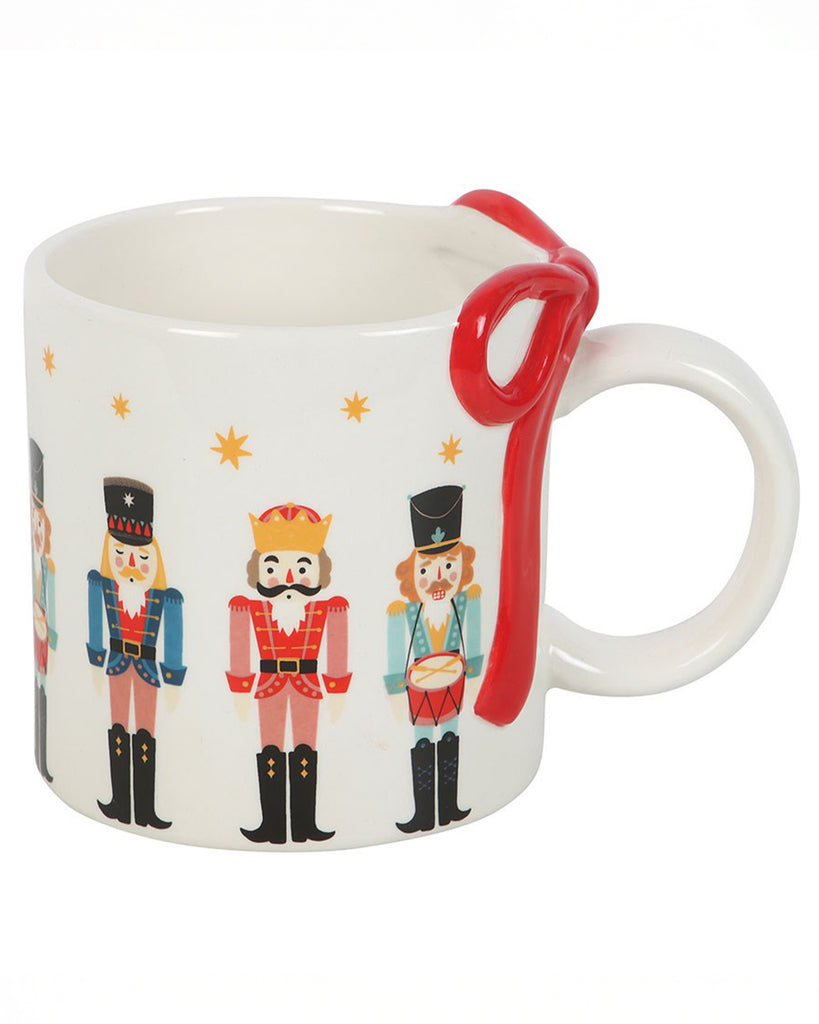 Close-up of Rebel Romance’s Nutcracker Print Mug with a white ceramic body, colourful nutcracker characters, yellow stars, and a red sculpted bow wrapped around the handle.