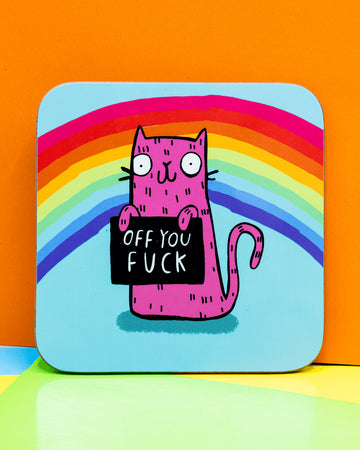 Colourful square coaster featuring a pink cartoon cat holding a black sign that says “Off You F*ck,” set against a light blue background with a rainbow arch. Designed by Katie Abey.