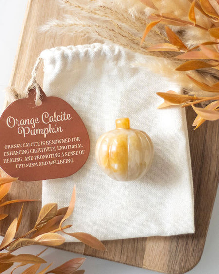 Orange Calcite Pumpkin
Alt text: A small, polished orange calcite crystal shaped like a pumpkin, placed on a cream drawstring pouch with a tag that reads, “Orange Calcite Pumpkin – renowned for enhancing creativity, emotional healing, and promoting wellbeing.” Surrounded by autumnal foliage and neutral decor.
