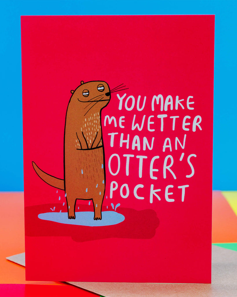 Bright pink greeting card by Rebel Romance featuring a quirky illustrated otter with water dripping off it, standing in a puddle. Bold white text reads "You make me wetter than an otter’s pocket." Designed by Katie Abey, this cheeky A6 card adds a fun and flirty touch to any gift. Ideal for Valentine’s Day, anniversaries, or playful notes. UK indie brand Rebel Romance specialises in alternative cards, gifts, and retro-inspired designs.